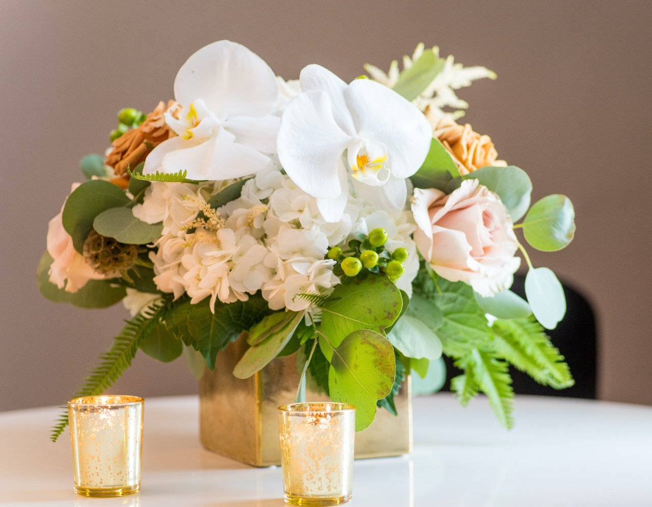 Bouquet of white flowers in a green vase on a wooden stool against a plain background