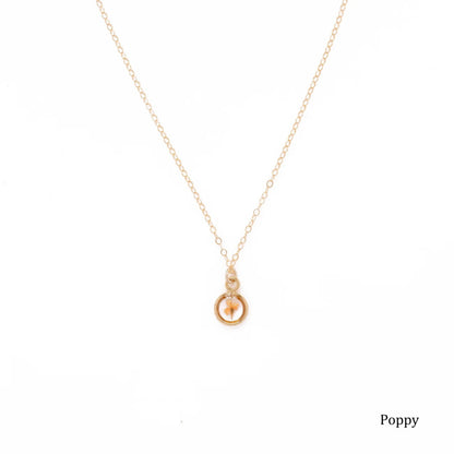 Gold necklace with a small round pendant with a dried poppy flower inside on a white background.
