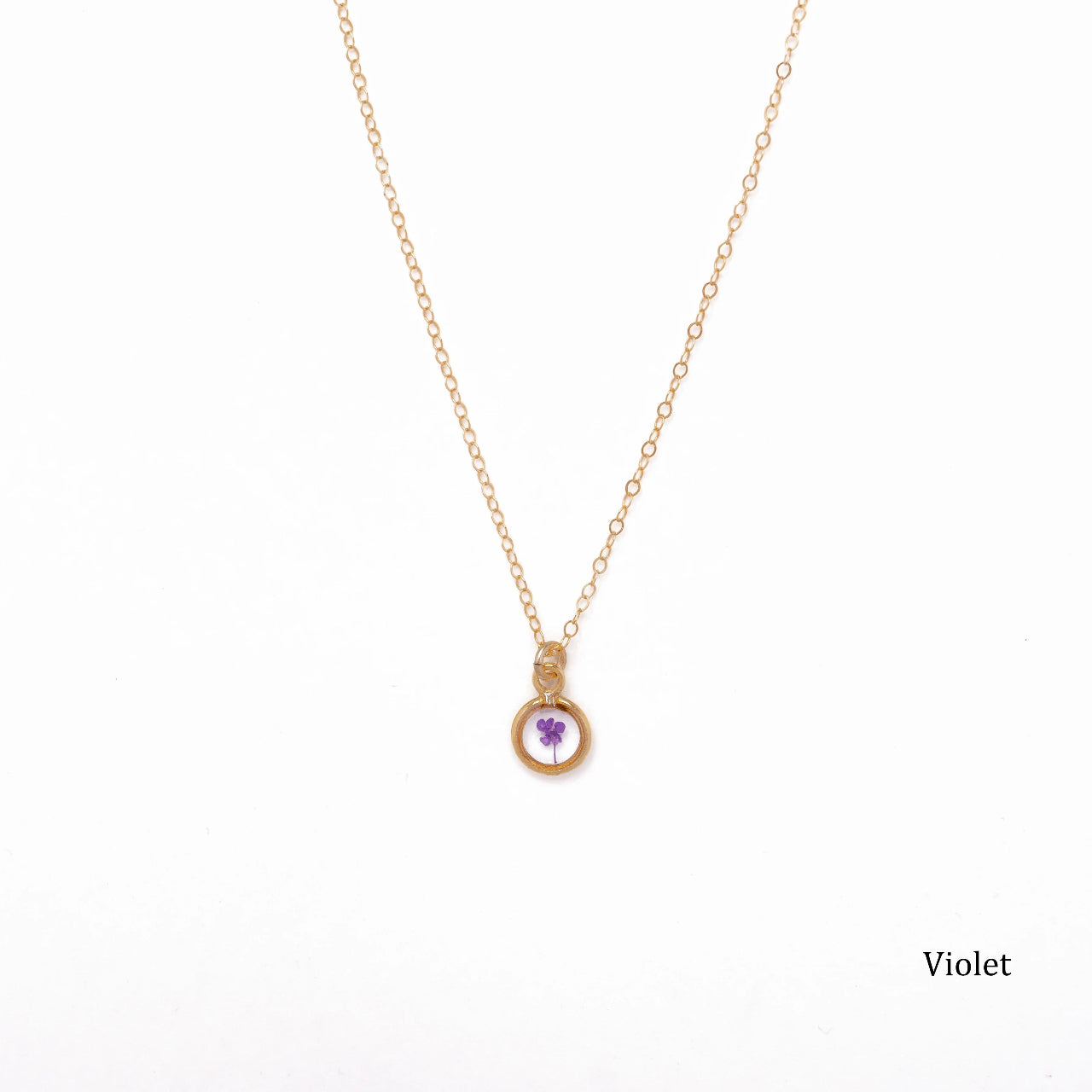 Gold necklace with a dried violet pendant on a white background