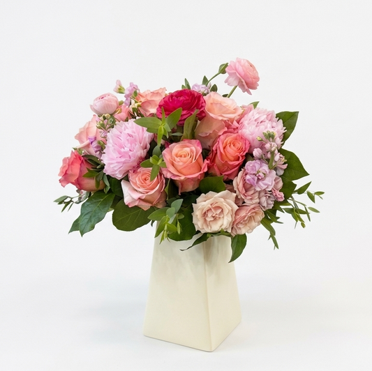 Bouquet of pink and peach flowers in a plastic lined cardboard vase on a white background