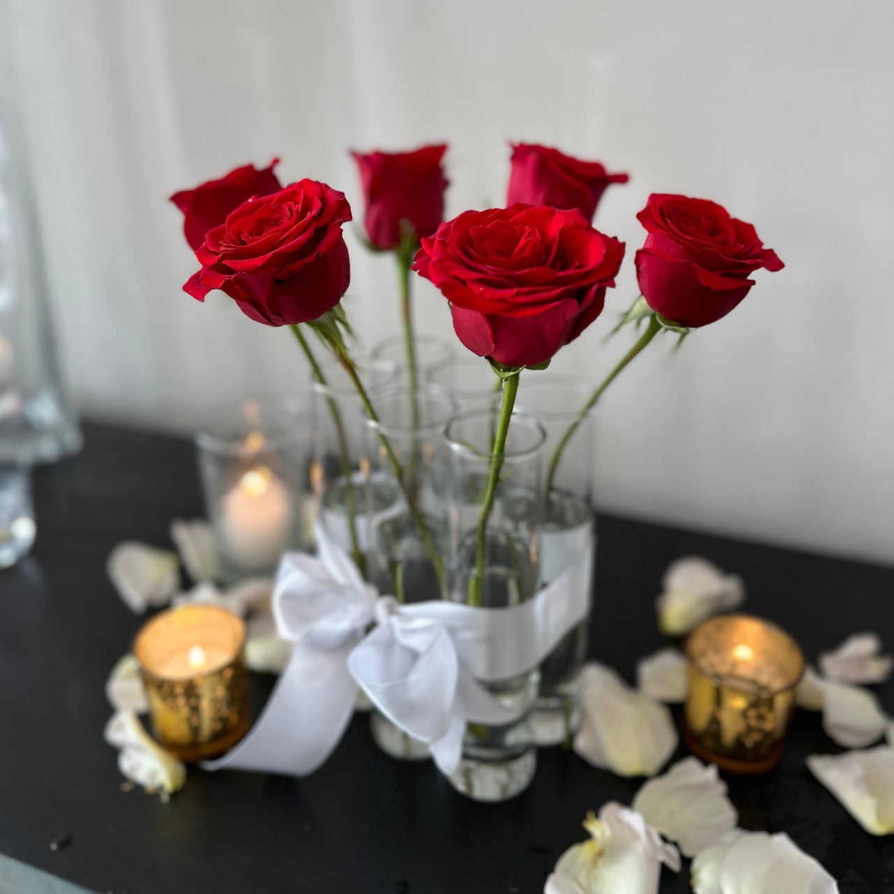 Sleek glass bud vases with red roses, grouped together as six pack tied with white ribbon