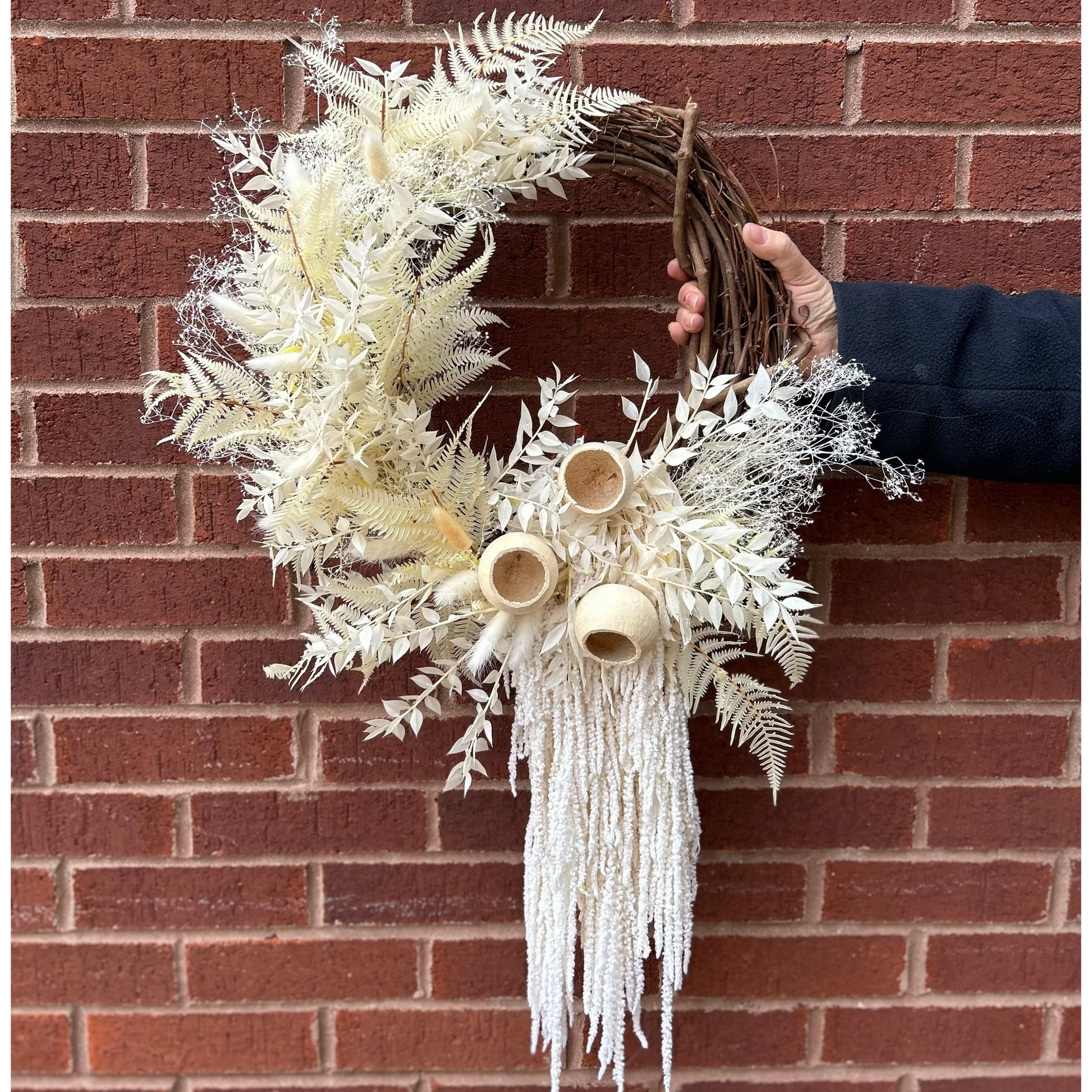 Decorative wreath with white foliage and dried floral elements against a brick wall.