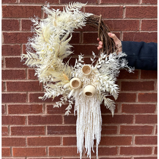 Decorative wreath with white foliage and dried floral elements against a brick wall.