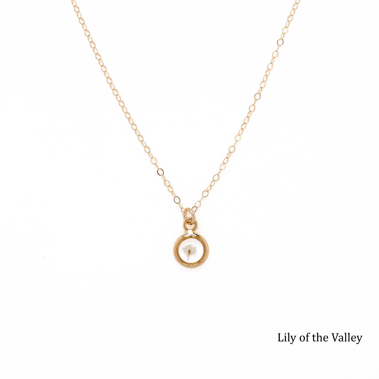 Gold necklace with a dried Lily of the Valley bud inside a pendant on a white background