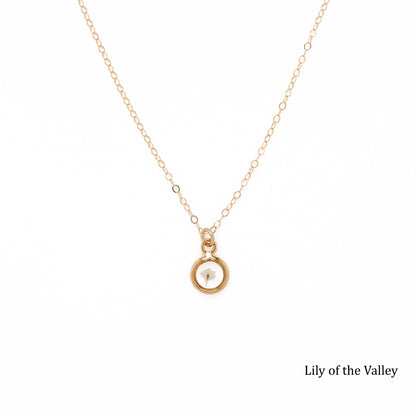 Gold necklace with a dried Lily of the Valley bud inside a pendant on a white background