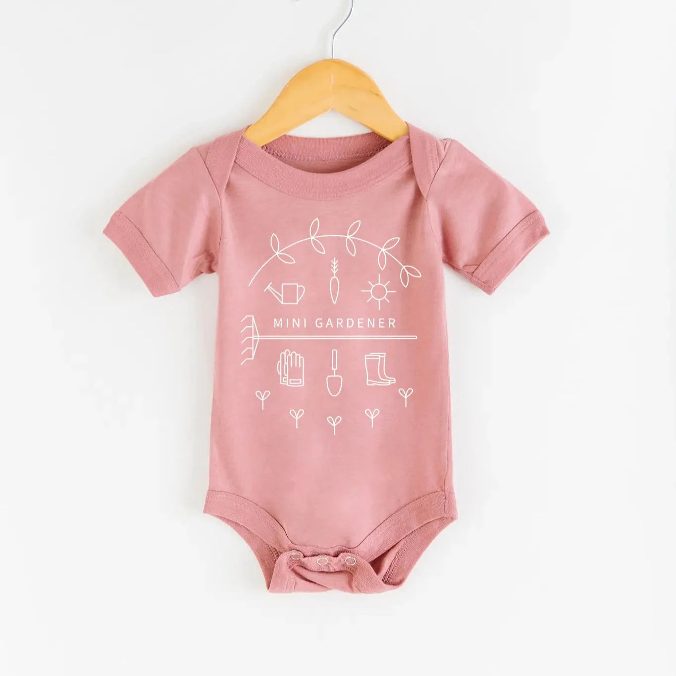 A pink baby bodysuit with gardening-themed graphics, designed for babies 6-12 months old, hanging on a hanger.