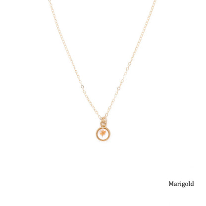Gold necklace with a small pendant with a dried marigold inside.