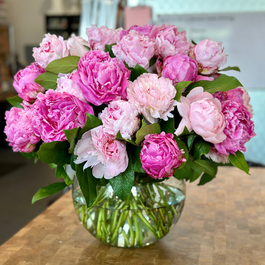 Bouquet of pink and white peonies in a clear vase on a wooden table.