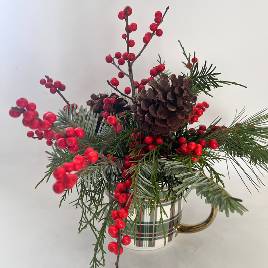 Decorative arrangement with red berries, pine cones, and greenery in a plaid mug on a white background