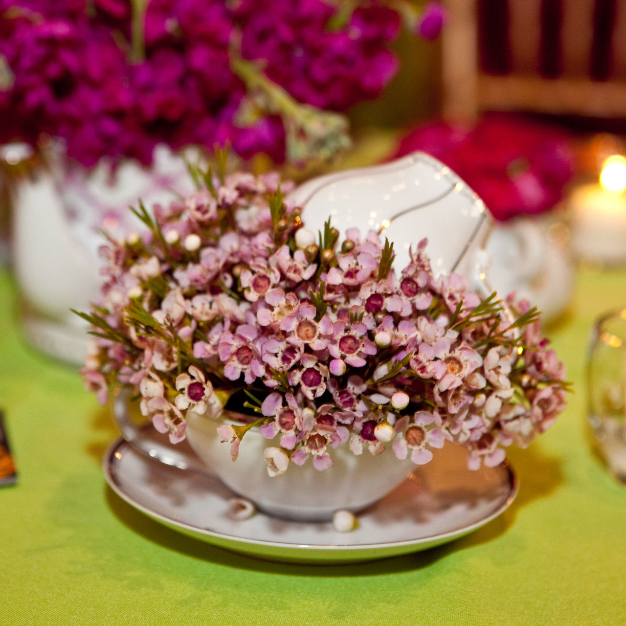 Decorative floral arrangement in a teacup on a table with candles and flowers.