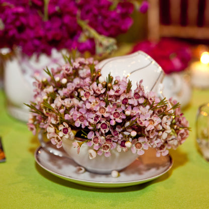 Decorative floral arrangement in a teacup on a table with candles and flowers.