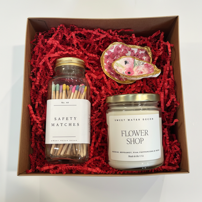 Gift set with a candle, matches, and decorative item in a box with red crinkle paper.