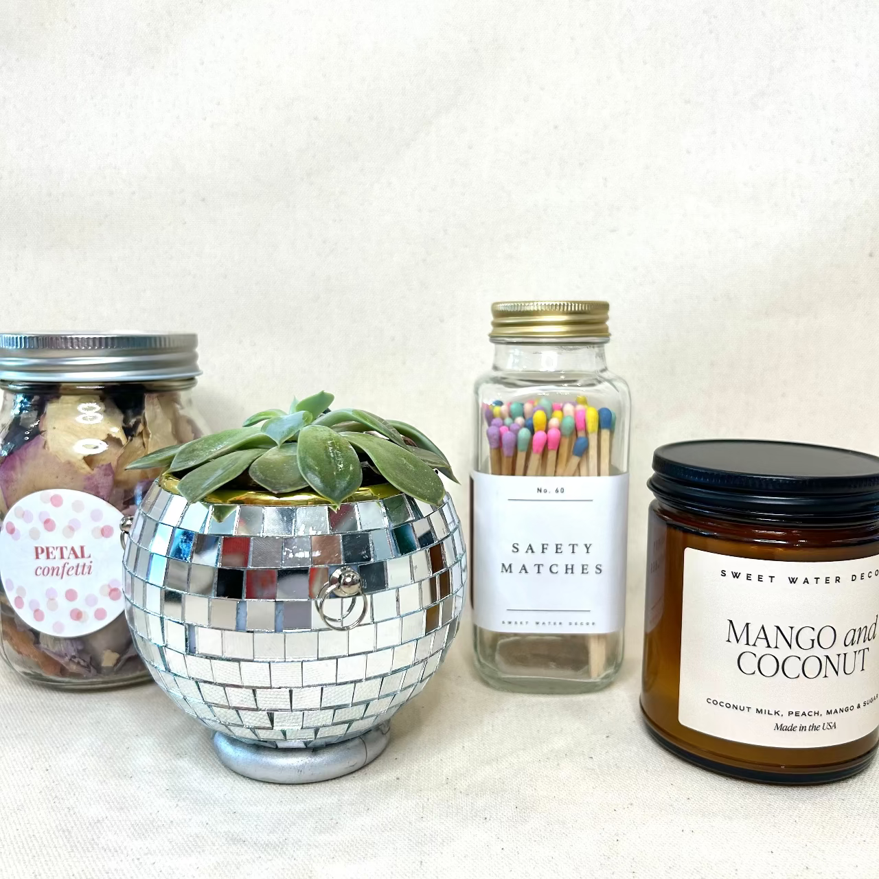 Decorative items including a disco ball planter, safety matches, and a candle on a white surface.