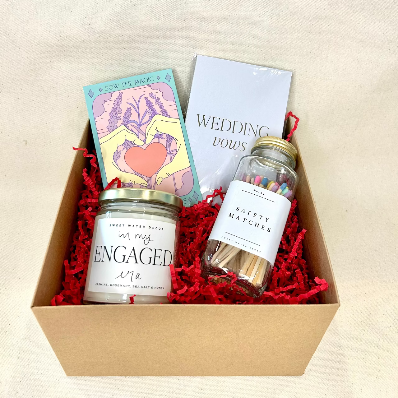 Gift box with 'Engaged' candle, matchbook, and safety matches on a beige background