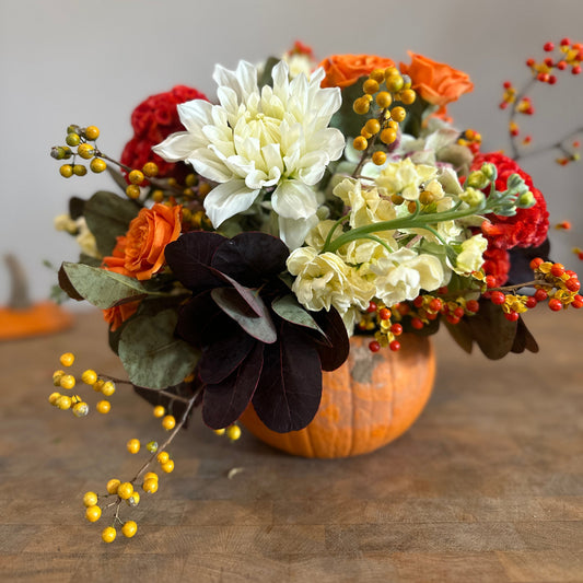 Decorative arrangement of flowers and berries in a pumpkin on a wooden surface.