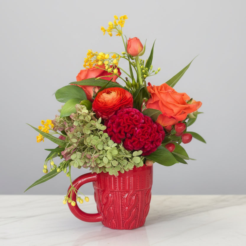 Floral arrangement in a red mug on a white surface