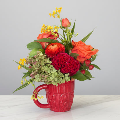 Floral arrangement in a red mug on a white surface