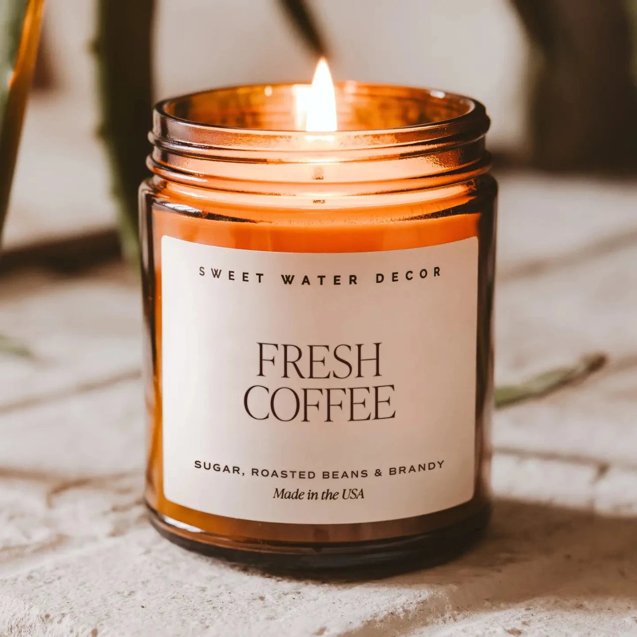 Candle in an amber jar labeled 'Fresh Coffee' by Sweet Water Decor on a neutral background.