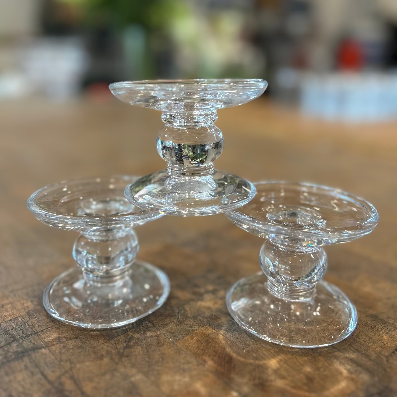 Three clear glass candle holders on a wooden surface with a blurred background