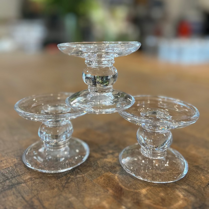 Three clear glass candle holders on a wooden surface with a blurred background