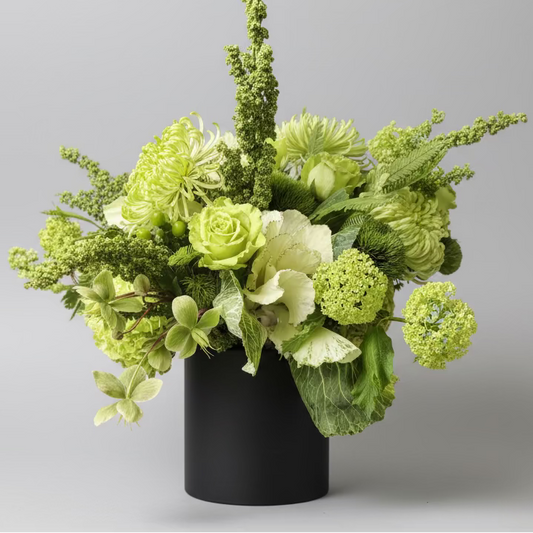 Green floral arrangement in a black vase on a wooden surface with a blurred background