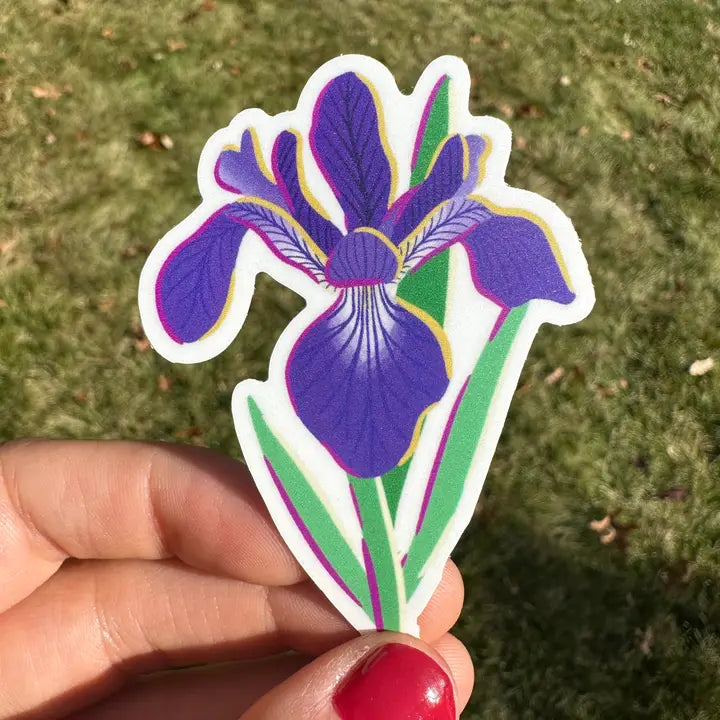A vinyl sticker with a floral design, predominantly pink, held between fingers, with a background of grass.