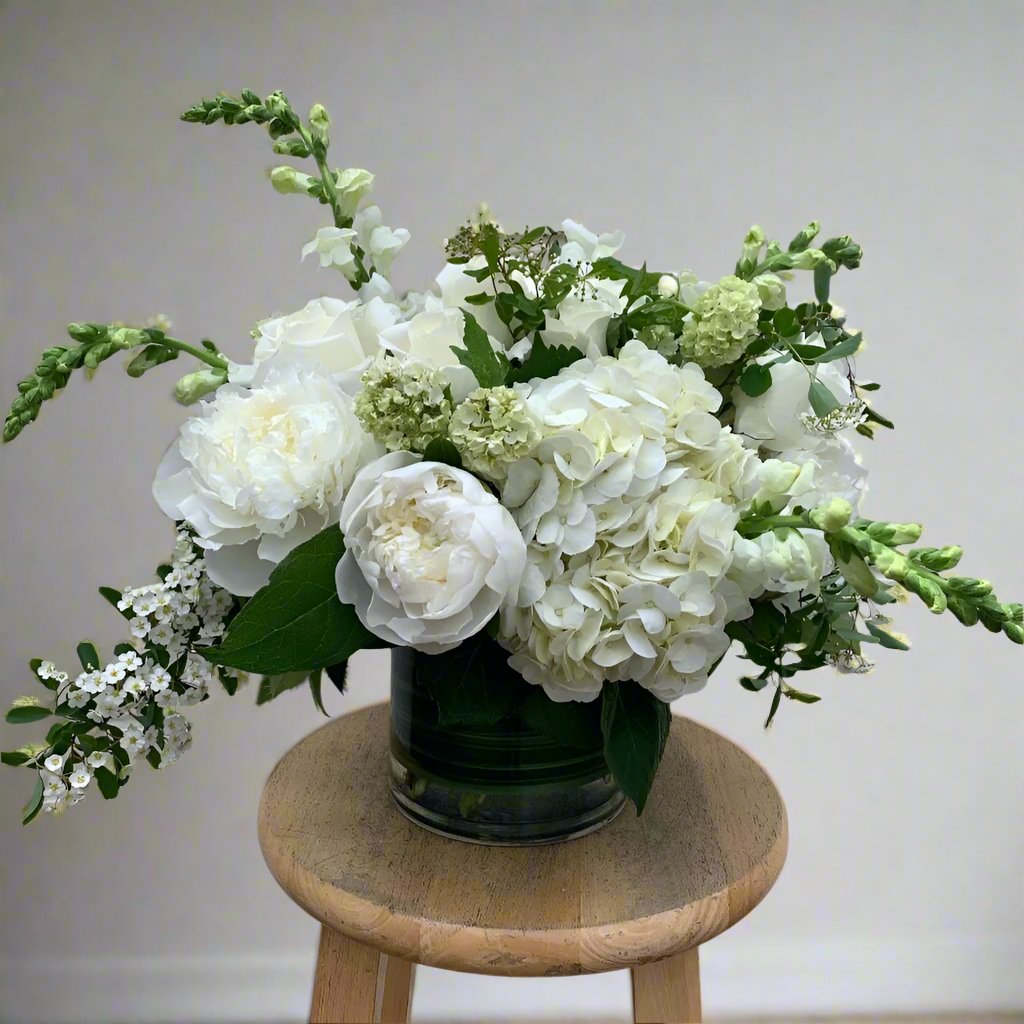 Bouquet of white flowers in a green vase on a wooden stool against a plain background
