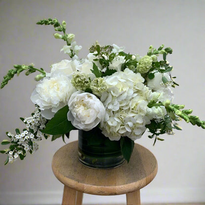 Bouquet of white flowers in a green vase on a wooden stool against a plain background