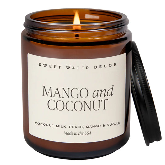 A mango and coconut scented soy candle in a brown jar with a label reading 'sweet water decor Mango and Coconut Coconut Milk, Peach, Mango & Sugar Made in the USA'.