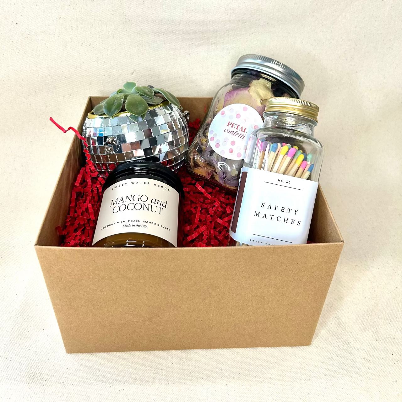 Gift box with mango and coconut candle, safety matches, and decorative items on a beige background