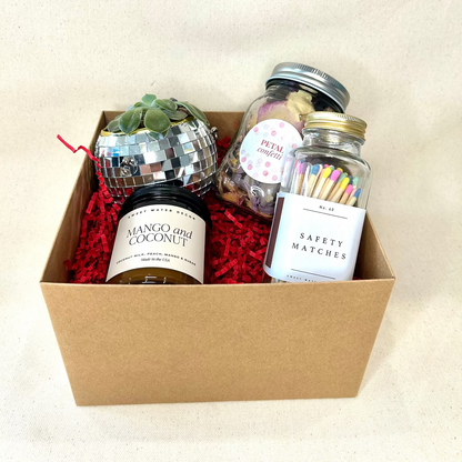 Gift box with mango and coconut candle, safety matches, and decorative items on a beige background