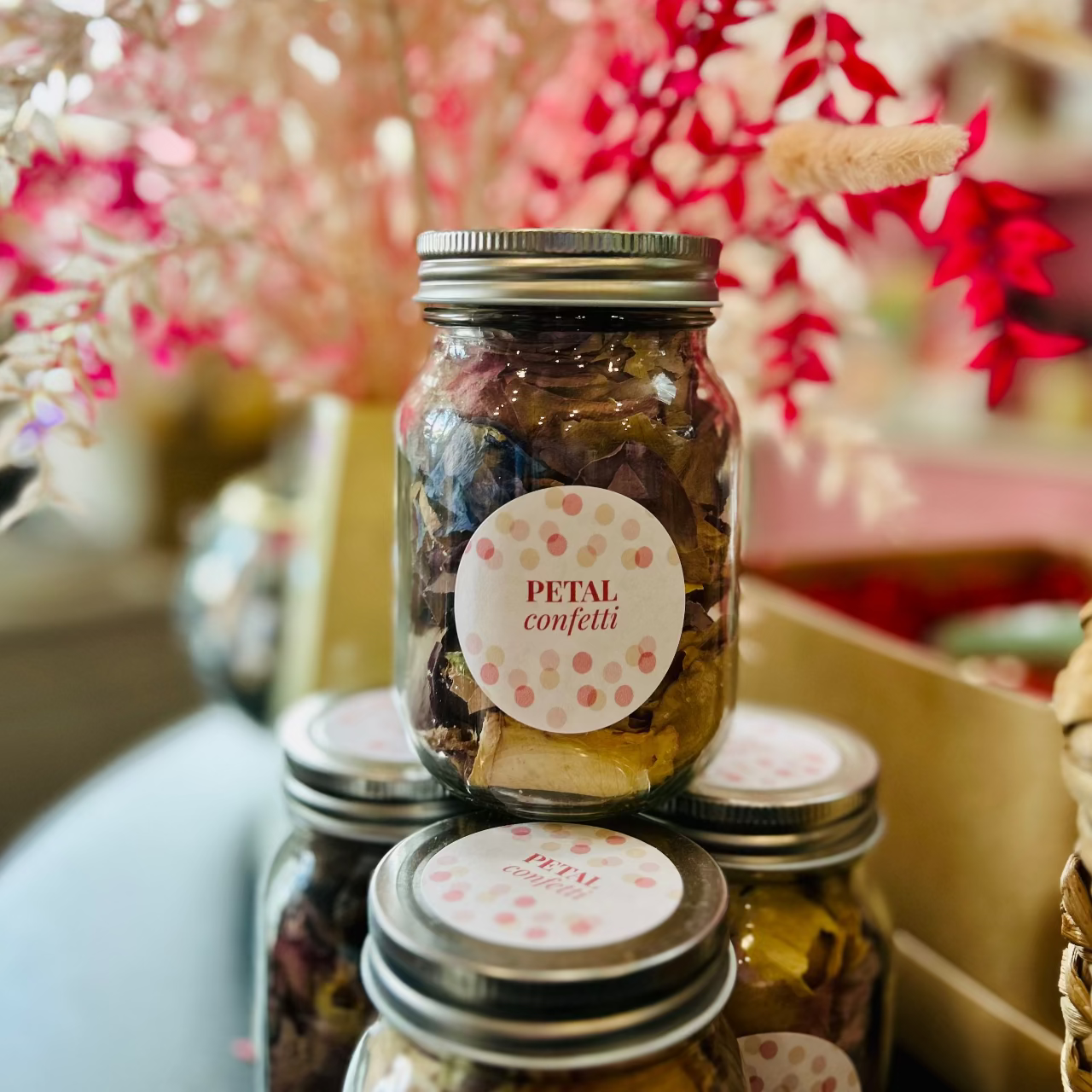 Jars of petal confetti with decorative labels on a blurred floral background