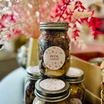 Jars of petal confetti with decorative labels on a blurred floral background