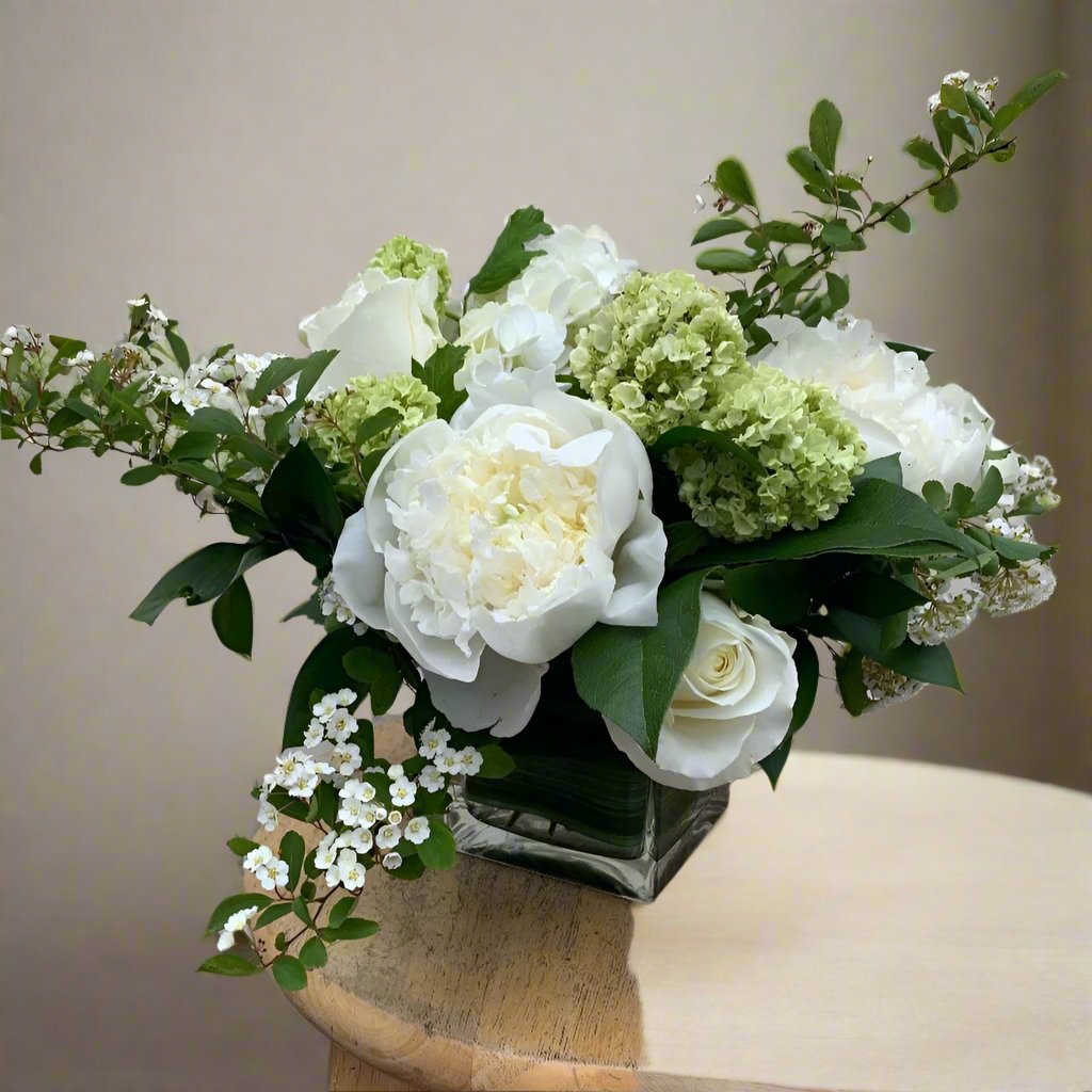 Bouquet of white and green flowers in a clear vase on a wooden surface with a neutral background