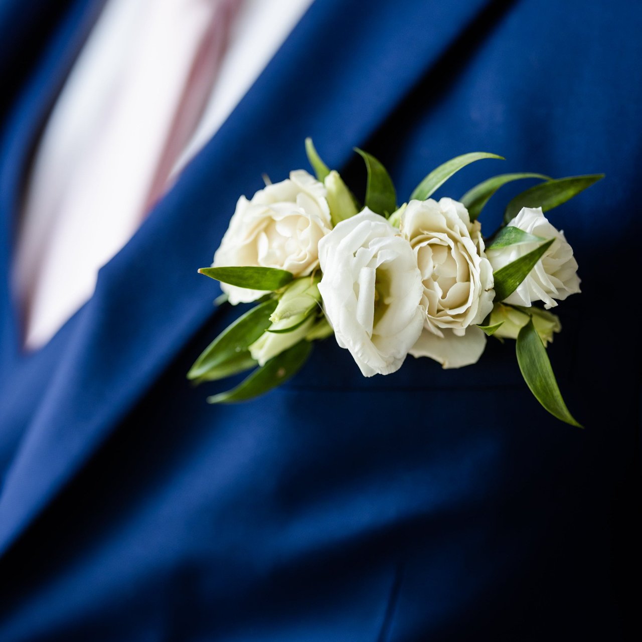 A close-up image of a man's blue suit jacket with a white and green floral pocket square attached to the lapel.