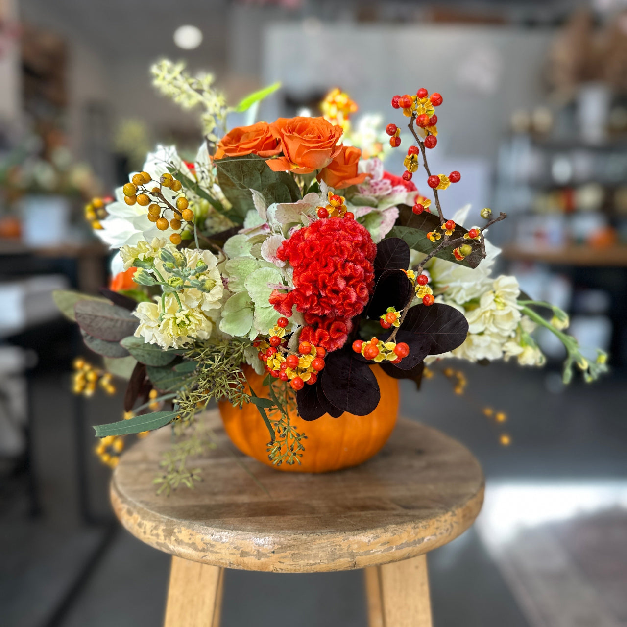 Floral arrangement in a pumpkin on a wooden stool with a blurred indoor background
