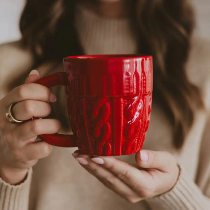 Red textured mug held by a person wearing a beige sweater.