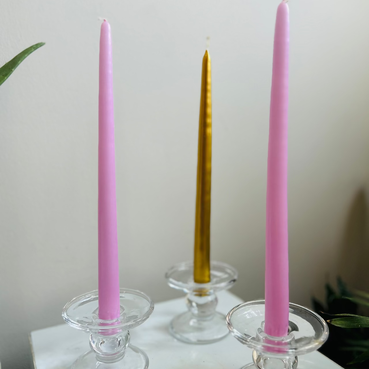 Three candlesticks with pink, gold, and purple candles on a white surface.