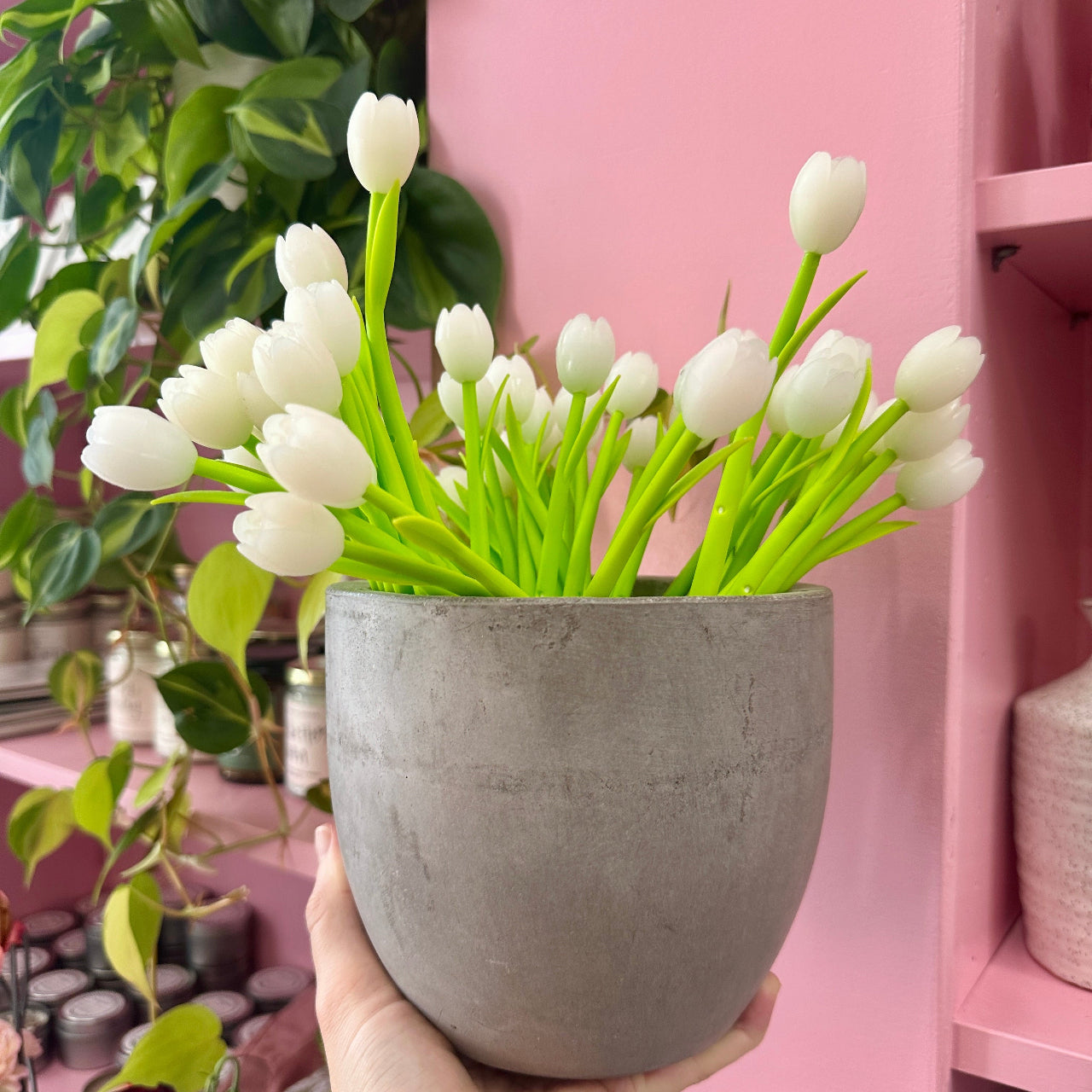 White tulip pens held by a hand against a pink background