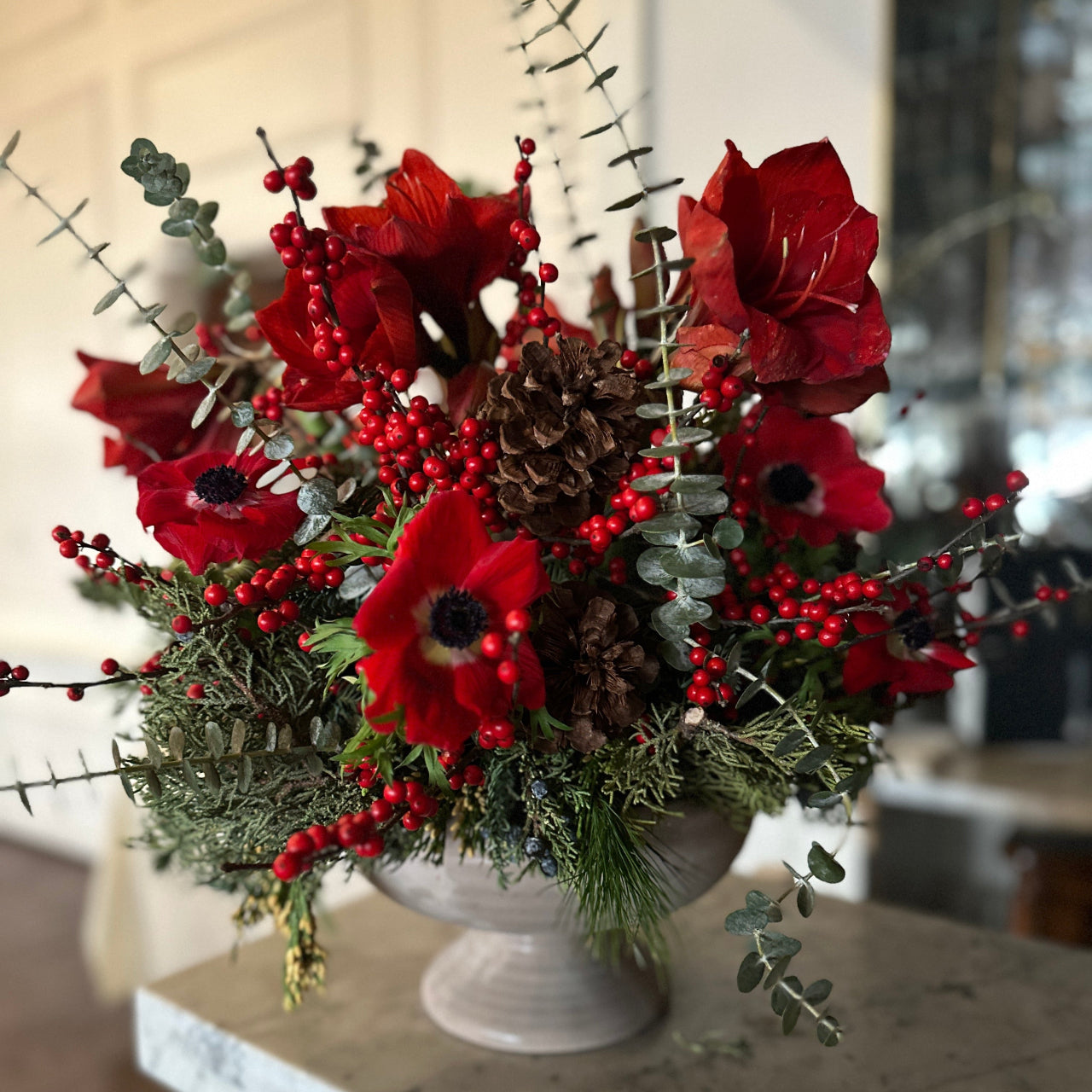 Decorative floral arrangement with red flowers, berries, and pinecones in a white vase.