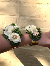 Load image into Gallery viewer, Two wrist corsages made from spray roses and texture, against a yellow brick wall. 
