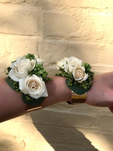 Two wrist corsages made from spray roses and texture, against a yellow brick wall. 