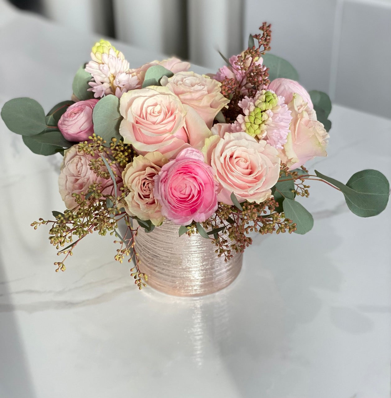This swoon worthy display features ranunculus, roses and tulips in delightful shades of pink. Fragrant pink hyacinth and touches of eucalyptus bring the design to love.